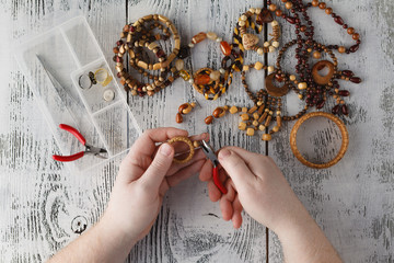 man making handmade jewelry. Boxes with beads, accessories for needlework on white wooden table....
