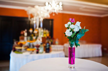 Flowers on vase with pink water at table of wedding guests.