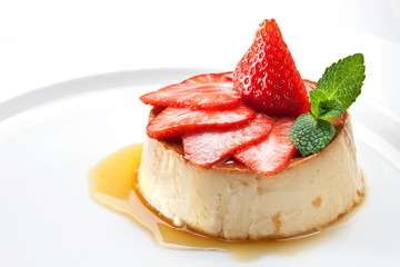  Milk pudding with caramel and strawberries on a white plate 