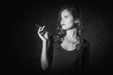 Noir film style woman in dress holding cigarette. Black and white photography. Old fashion photo