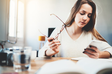 Young beautiful woman using smartphone device at home interior, attractive female freelancer working at modern co working space reading financial statistics in the advertising market in internet