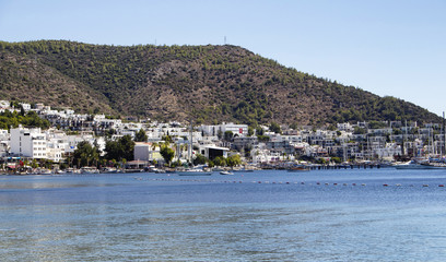 Fototapeta na wymiar Luxury yachts and sail boats parked in front of Bodrum - Icmeler city in a sunny summer day. The city is on the Bodrum Peninsula, stretching from Turkey's southwest coast into the Aegean Sea.