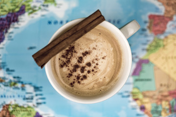 Cup of coffee with quill of cinnamon over world map blurred in background