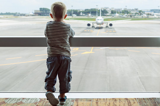 Little baby boy waiting boarding to flight in airport transit hall and looking through the window at airplane near departure gate. Active family lifestyle, travel by air with child on summer vacation
