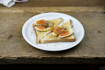 Open sandwich with seasoned hard boiled egg on sliced white bread served on a rustic wooden table