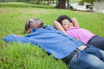 African American Young man and little kid relaxing and looking at clouds on green park