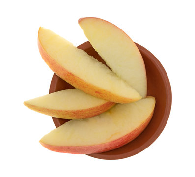 Top view of red apple slices in a small clay bowl isolated on a white background.