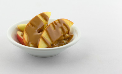 Apple slices covered with peanut butter in a bowl offset on a white tablecloth.