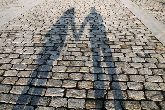 Shadows of a loving couple holding hands in the city center on cobblestones on a sunny day.