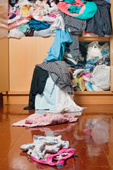 Messy disorder clothes over the closet. Untidy cluttered woman clothes scattered on the wood floor.