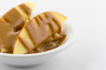 Apple slices covered with peanut butter on a white tablecloth close view.