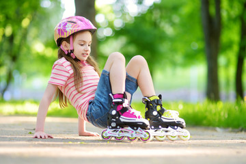 Pretty little girl learning to roller skate on beautiful summer day in a park