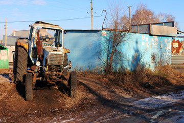 An old broken rusted tractor in the Russian village against a blue sky