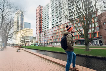 Fotobehang A young guy dressed warmly examines the city in the morning in rainy weather. Rotterdam, Netherlands. © Lalandrew