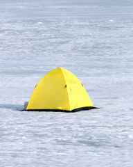 Fisherman tent from yellow with black bottom in snow on frozen river in winter day vertical view