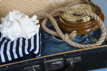 holidays concept/old suitcase with jeans, striped clothes, barometer and sea shell