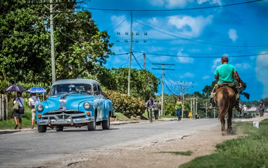 Blauer amerikanischer Oldtimer mit einem Reiter auf der Landstraße nach Santa Clara - Serie Kuba Reportage