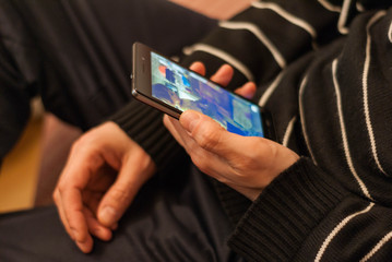 A young man sitting on the couch to rest with a smartphone in hand.