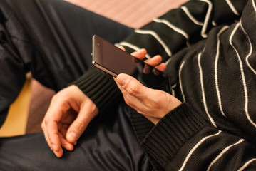 A young man sitting on the couch to rest with a smartphone in hand.