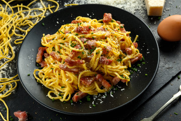 Classic Homemade Pasta carbonara Italian with Bacon, eggs, Parmesan Cheese on black plate.