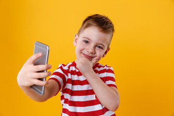 Fototapeta premium Smiling little boy making selfie and thinking about something