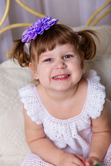 A little girl in a white knitted dress pampered on a bed