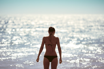 Fashion shot of young beautiful brunette girl in black bikini standing on beach.