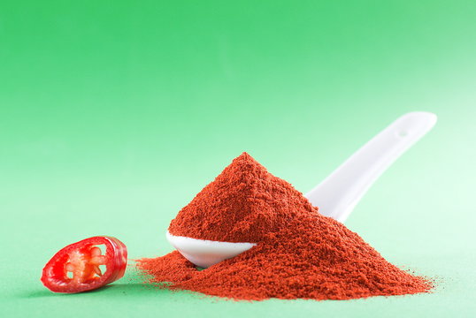 Ground red pepper in a white spoon on a green background
