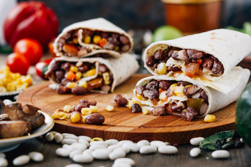 Nice vegetarian burrito over black table on wooden board.