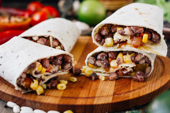 Nice vegetarian burrito over black table on wooden board.