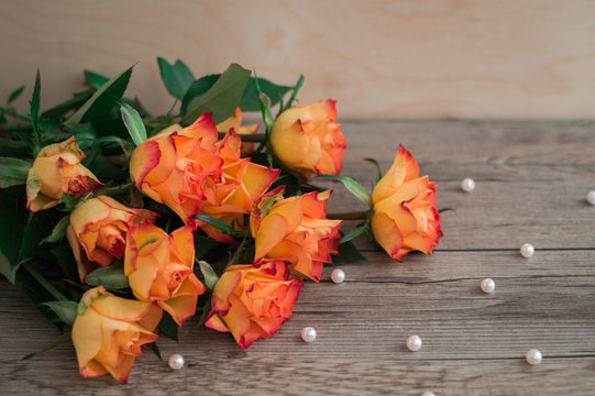 Orange roses on a wooden background and scattered beads of pearls. A beautiful bouquet of roses. The best present on birthday. 