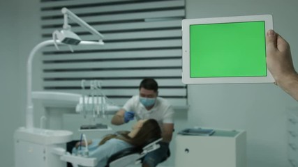 Tablet pc, on background of working male dentist and lying female patient. - Powered by Adobe