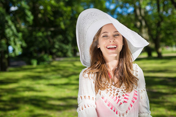 Beautiful woman in hat standing in park laughing