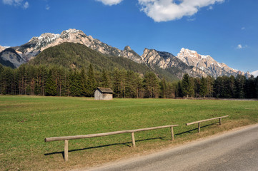 Landscape of Dolomites mountains in summer with a farm and meadows near a fence