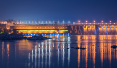 Dam at night. Beautiful industrial landscape with dam hydroelectric power station, bridge, river, city illumination reflected in water, rocks and sky. Dniper River, Zaporizhia, Ukraine.