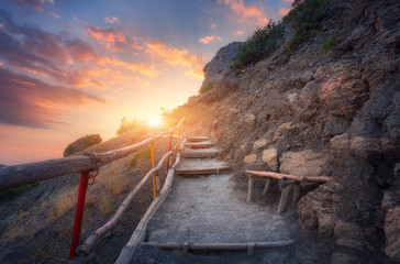Stone stairs with wooden railing in the mountains at sunset. Landscape with mountain path and rocks...