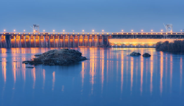 Dam at night. Beautiful industrial landscape with dam hydroelectric power station, bridge, river, city illumination reflected in water, rocks and sky. Dniper River, Zaporizhia, Ukraine.