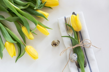 Easter concept with copy space. Decorative easter place setting with yellow tulip, a quail egg on a white background.