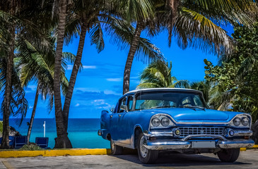 Blauer amerikanischer Oldtimer parkt am Strand unter Palmen in Varadero Kuba - Serie Kuba Reportage - obrazy, fototapety, plakaty