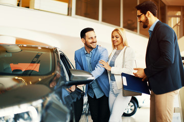 Young couple choosing new car for buying in dealership shop