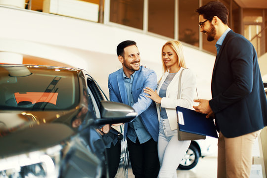 Young Couple Choosing New Car For Buying In Dealership Shop