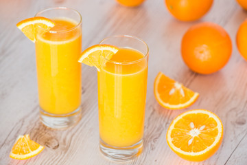 orange juice in glasses at light wooden background