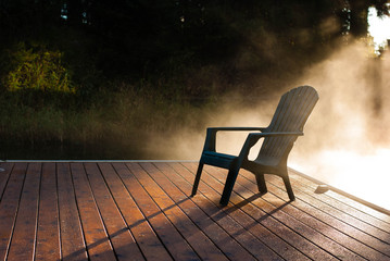 Adirondack chair on dock with fog at sunrise.