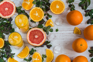 orange juice with ice in glasses near citrus and mint at light wooden background