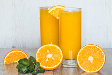 orange juice with mint in glasses at light wooden background