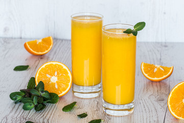 Fototapeta na wymiar orange juice with mint in glasses at light wooden background