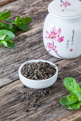 Green dry tea flavored with mint on wood spoon on wooden background