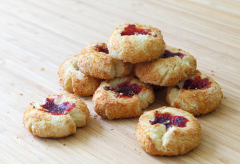 A batch of coconut cookies with raspberry jam filling on a wooden table.