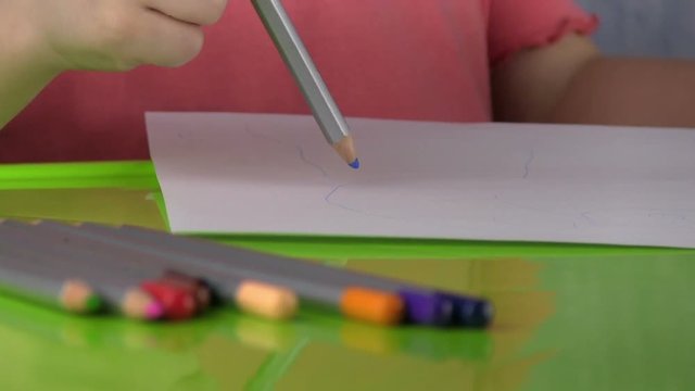 Pencils Lying On A Green Table. On the Backround Little Girl Draws