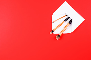 Make up brushes with white open envelope on red background